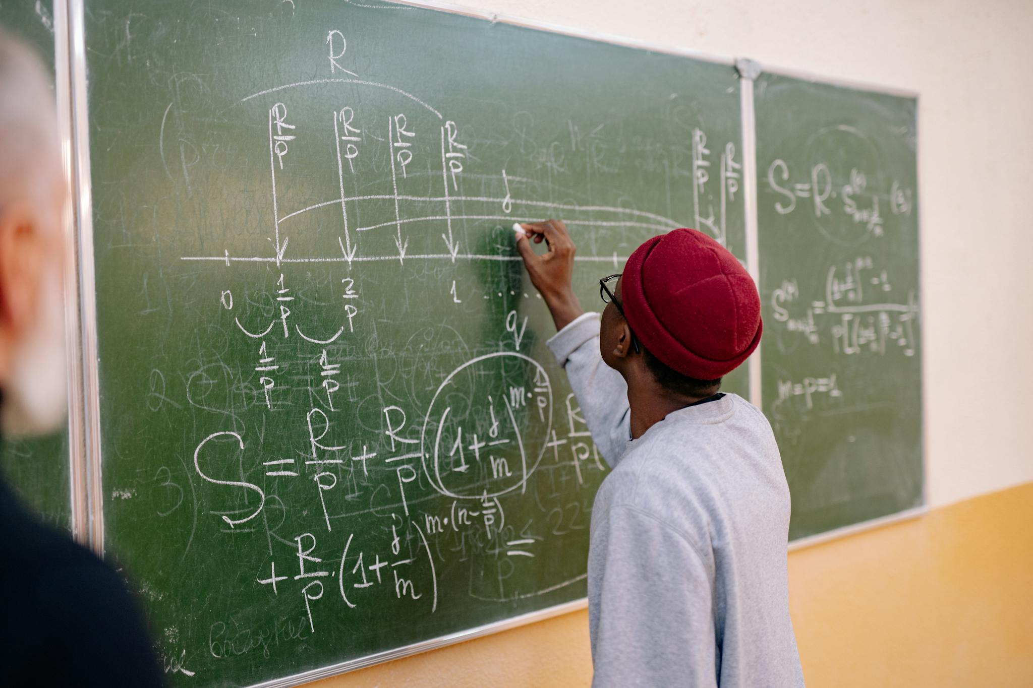 A young student writes mathematical equations on a green blackboard with precision and focus.
